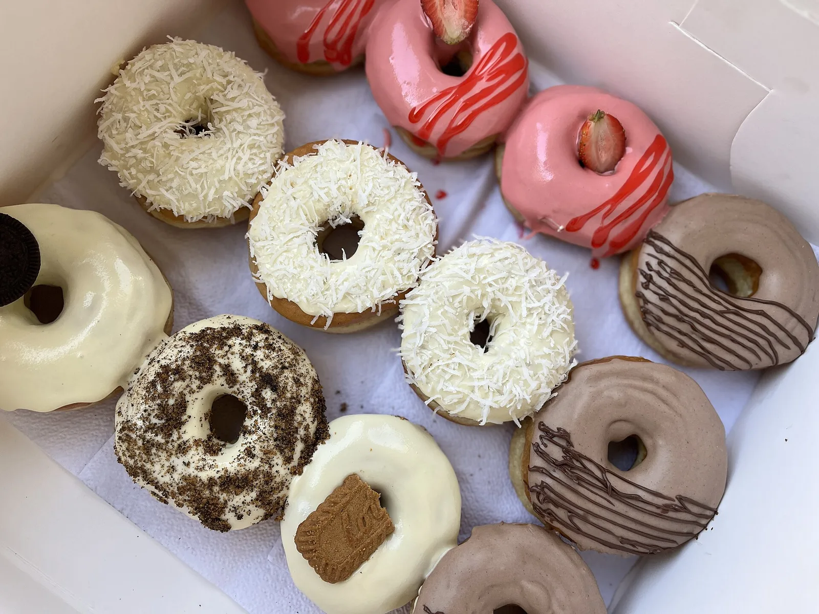 A tray of glazed ring doughnuts in strawberry, coconut, chocolate and milk flavors.