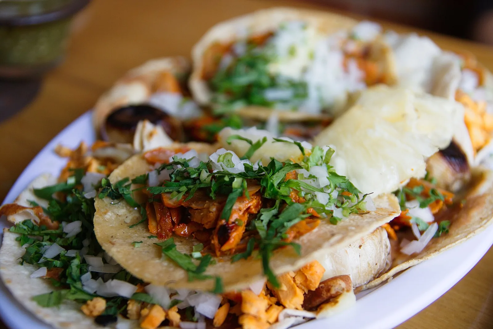 A plate of tacos al pastor topped with onion and cilantro.
